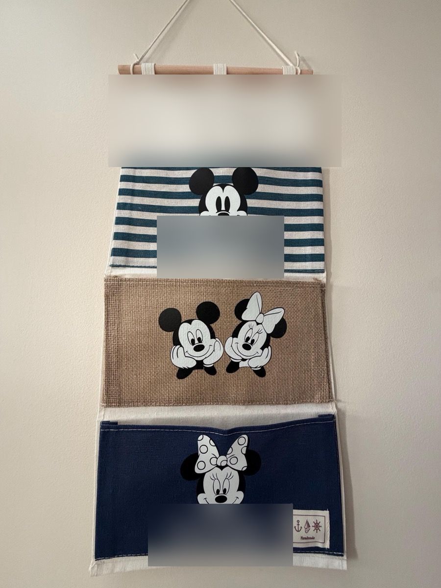 A fish extender with navy-stripe, burlap and denim pockets showing Mickey and Minnie, hanging on a wall